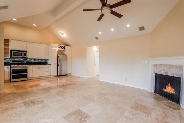 kitchen featuring ceiling fan, appliances with stainless steel finishes, a tiled fireplace, tasteful backsplash, and high vaulted ceiling