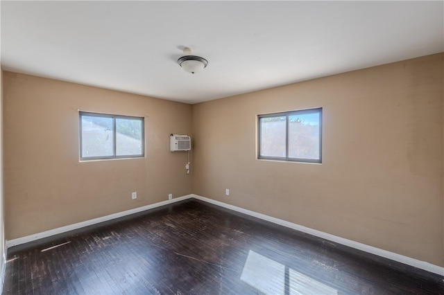 empty room with a wall mounted AC, a wealth of natural light, and dark hardwood / wood-style floors