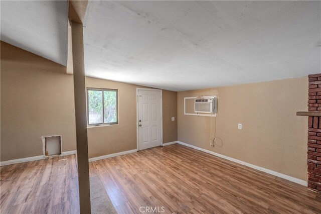 foyer entrance with light hardwood / wood-style floors, lofted ceiling, and an AC wall unit