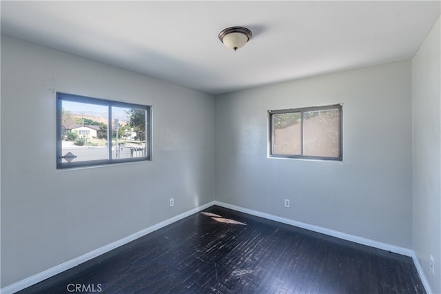 spare room featuring a healthy amount of sunlight and dark hardwood / wood-style flooring