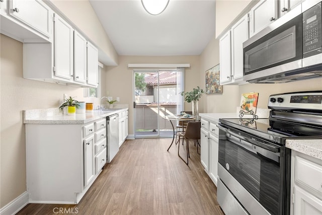 kitchen with appliances with stainless steel finishes, light wood-type flooring, sink, and white cabinets