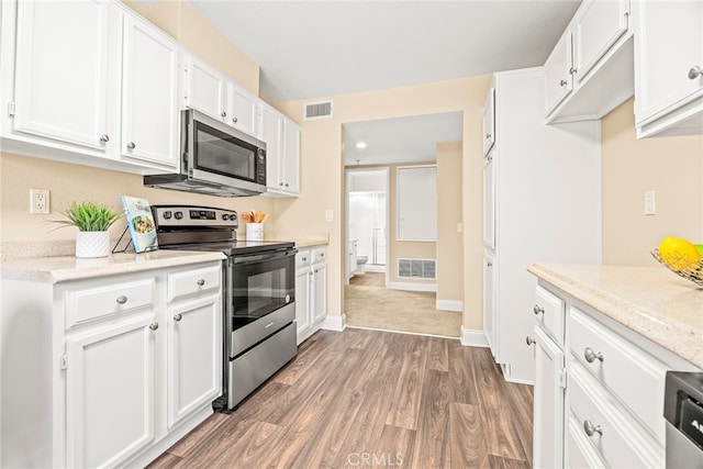 kitchen featuring appliances with stainless steel finishes, light stone countertops, dark wood-type flooring, and white cabinets