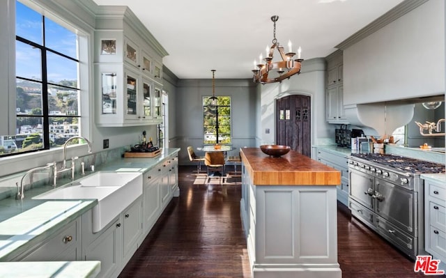 kitchen with high end stainless steel range, a center island, wooden counters, decorative light fixtures, and sink