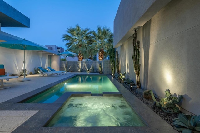 pool at dusk featuring an in ground hot tub and a patio area