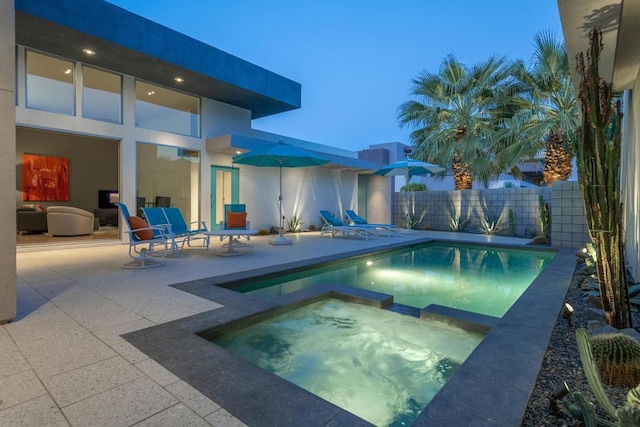 pool at dusk featuring an in ground hot tub and a patio