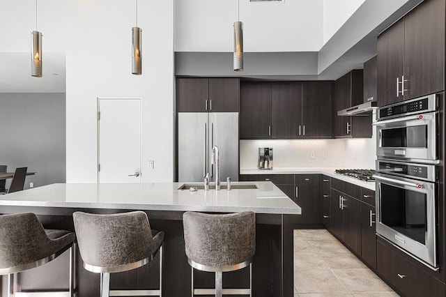 kitchen featuring hanging light fixtures, appliances with stainless steel finishes, a center island with sink, and a kitchen breakfast bar