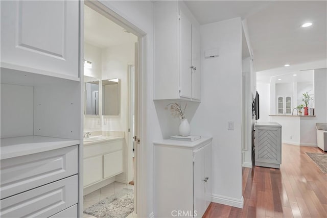 interior space featuring recessed lighting, a sink, baseboards, and wood finished floors