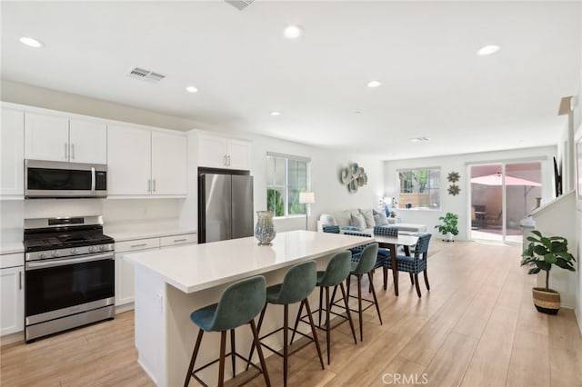 kitchen with white cabinets, light hardwood / wood-style flooring, appliances with stainless steel finishes, a kitchen breakfast bar, and a center island