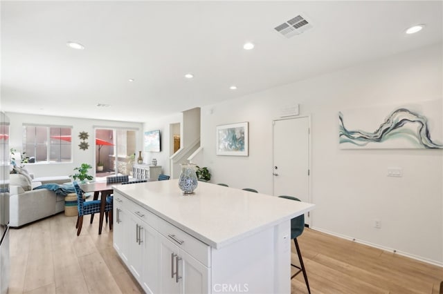 kitchen featuring light hardwood / wood-style flooring, white cabinets, a center island, and a breakfast bar area