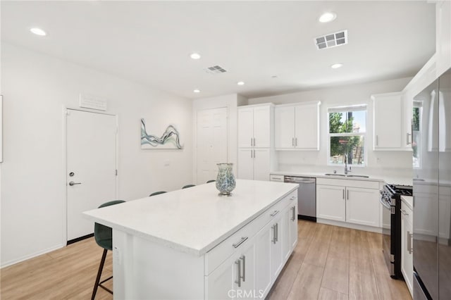 kitchen featuring light hardwood / wood-style floors, white cabinets, a kitchen island, stainless steel appliances, and sink