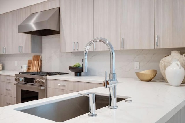 kitchen with tasteful backsplash, stainless steel stove, wall chimney exhaust hood, and light brown cabinets