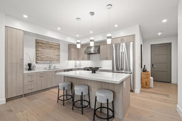 kitchen with pendant lighting, sink, stainless steel appliances, a kitchen island, and wall chimney exhaust hood