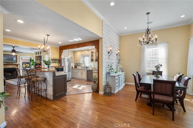 dining space with ceiling fan with notable chandelier, wood-type flooring, and ornamental molding