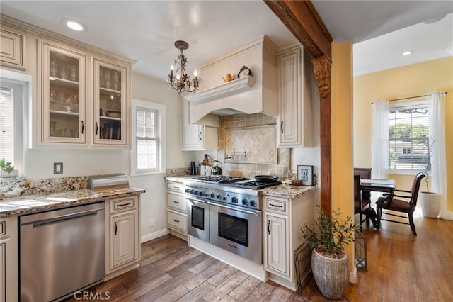 kitchen with light stone countertops, stainless steel appliances, dark hardwood / wood-style flooring, cream cabinets, and pendant lighting