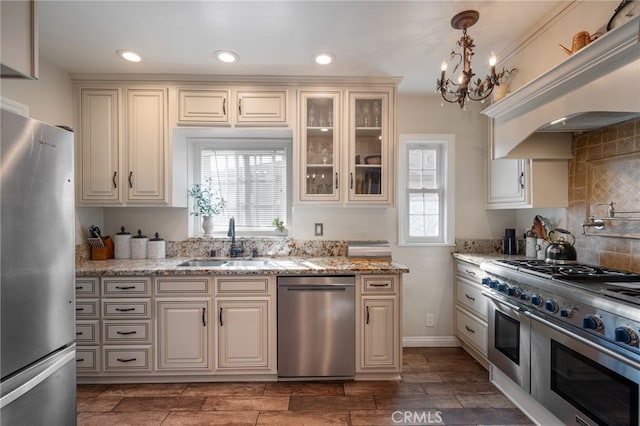 kitchen with light stone counters, hanging light fixtures, sink, and stainless steel appliances