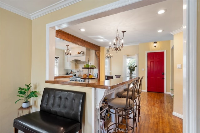 kitchen with ornamental molding, decorative light fixtures, light hardwood / wood-style flooring, and a breakfast bar area