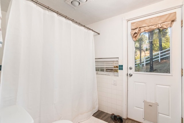 bathroom with wood-type flooring, a textured ceiling, a shower with curtain, tile walls, and toilet