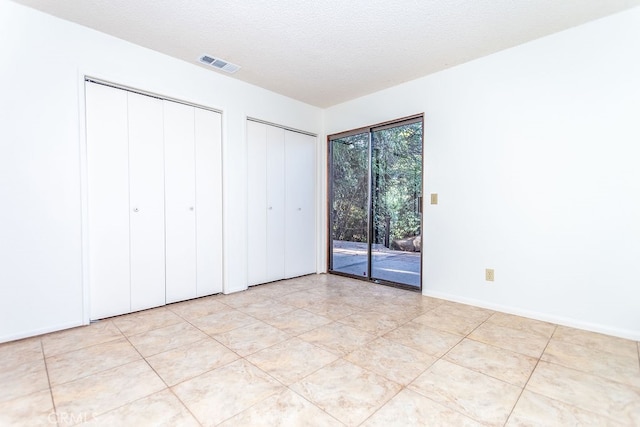 unfurnished bedroom with access to outside, multiple closets, a textured ceiling, and light tile patterned floors