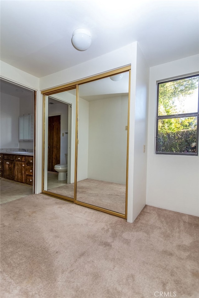 unfurnished bedroom featuring ensuite bath, light carpet, and a closet