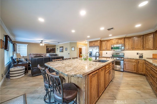 kitchen with light stone countertops, a kitchen bar, stainless steel appliances, sink, and a kitchen island with sink