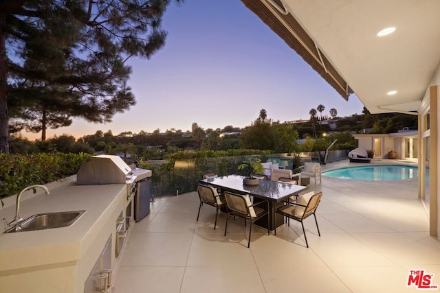 patio terrace at dusk with area for grilling, sink, and exterior kitchen