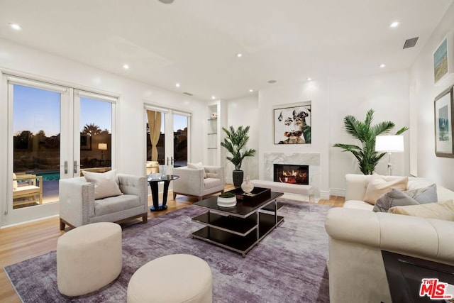 living room featuring a high end fireplace, french doors, and light hardwood / wood-style flooring