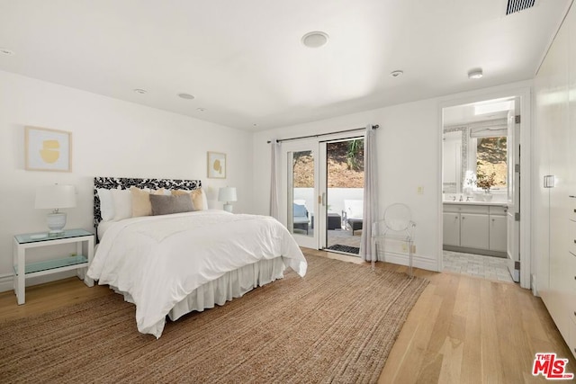 bedroom with multiple windows, light hardwood / wood-style floors, ensuite bath, and access to exterior