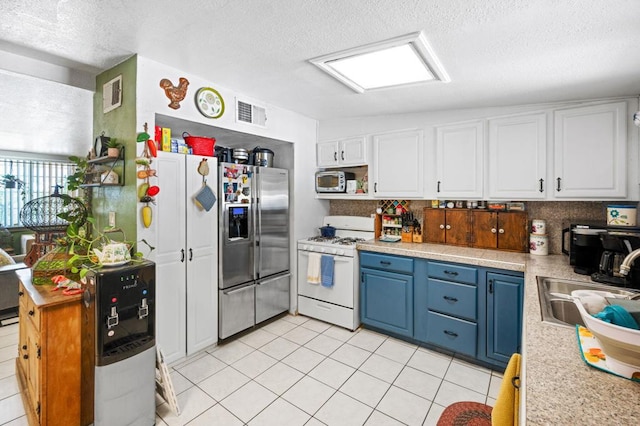 kitchen with appliances with stainless steel finishes, light tile patterned flooring, white cabinets, blue cabinetry, and sink