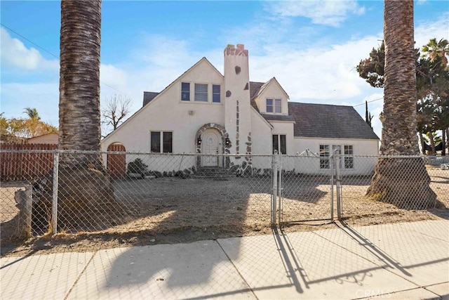 rear view of house featuring a gate, a fenced front yard, a chimney, and stucco siding