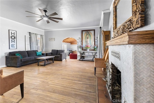 living room featuring hardwood / wood-style flooring, ceiling fan, ornamental molding, and a fireplace