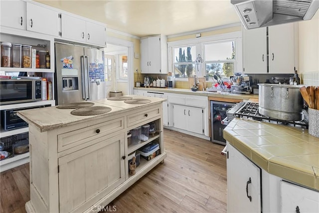 kitchen featuring appliances with stainless steel finishes, white cabinets, a center island, exhaust hood, and light hardwood / wood-style flooring