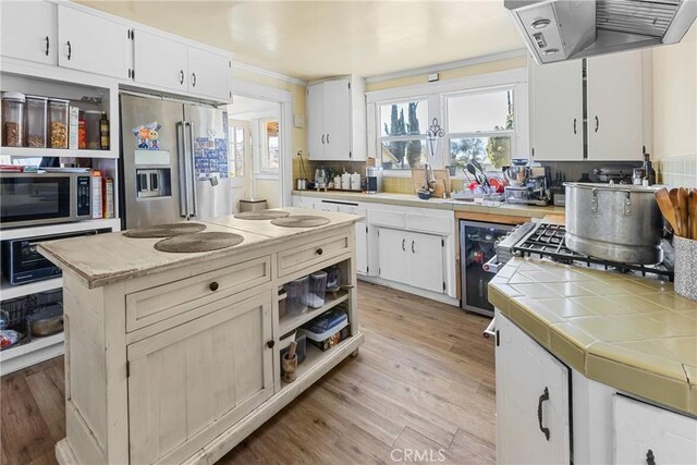 41695 Mayberry Ave, Hemet, CA 92544 - kitchen with appliances with stainless steel finishes, extractor fan, tile countertops, beverage cooler, and white cabinets