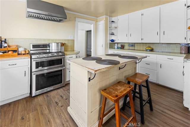 kitchen with wall chimney range hood, double oven range, a kitchen breakfast bar, tasteful backsplash, and white cabinets