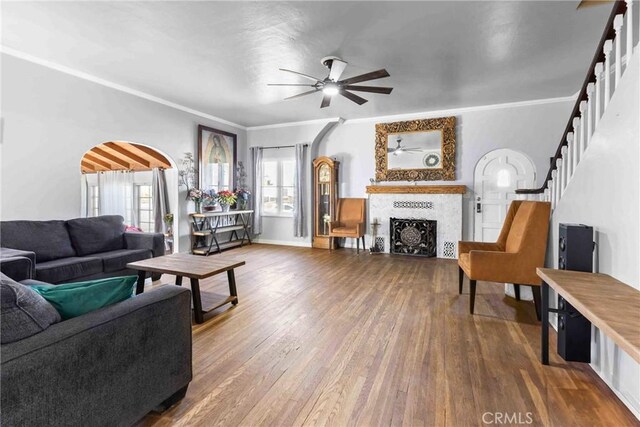 living room featuring a tiled fireplace, crown molding, wood-type flooring, and ceiling fan