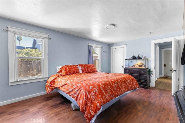 bedroom with multiple windows, wood finished floors, and baseboards