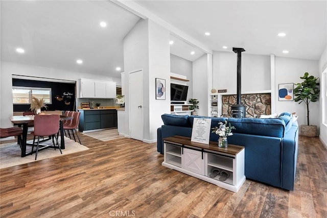 living room with beamed ceiling, high vaulted ceiling, a wood stove, and hardwood / wood-style flooring