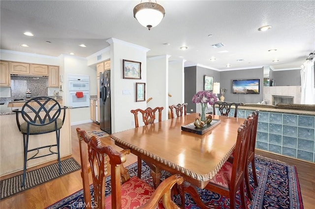 dining space with hardwood / wood-style floors, crown molding, a fireplace, and a textured ceiling