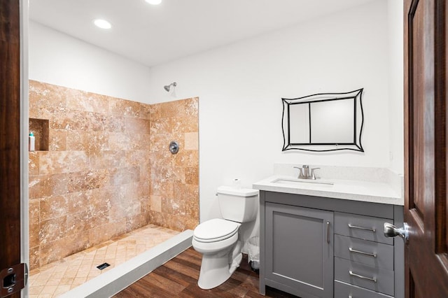 bathroom featuring hardwood / wood-style floors, vanity, toilet, and a tile shower