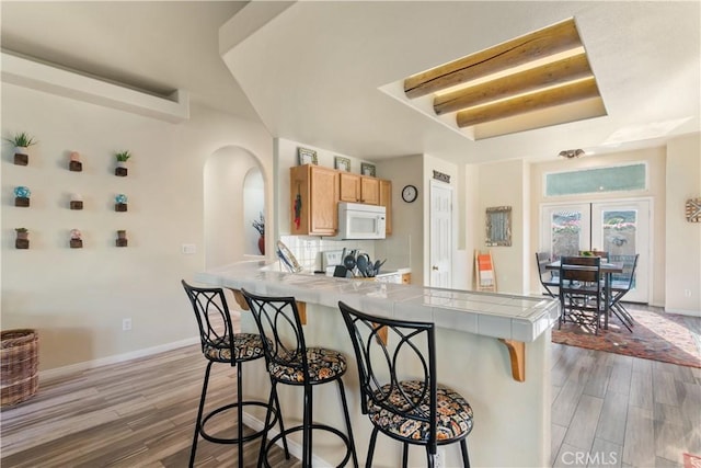 kitchen featuring electric range, french doors, tile countertops, light hardwood / wood-style floors, and a breakfast bar area