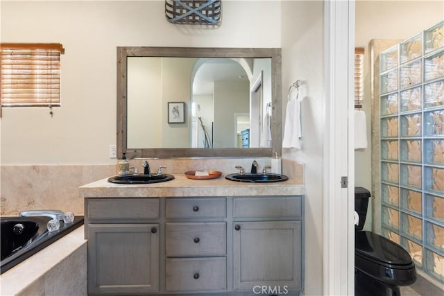 bathroom featuring vanity, toilet, and tiled bath