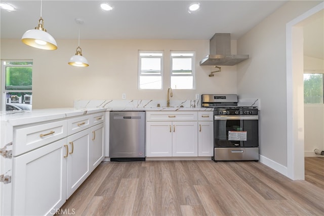 kitchen with appliances with stainless steel finishes, light hardwood / wood-style floors, wall chimney exhaust hood, white cabinets, and light stone counters