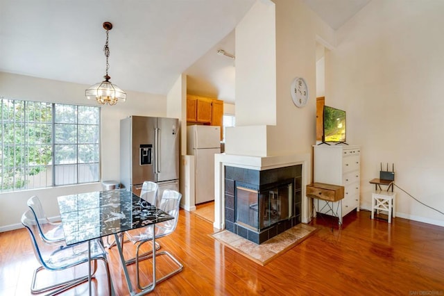 dining area featuring high vaulted ceiling, light wood-type flooring, a tile fireplace, and an inviting chandelier