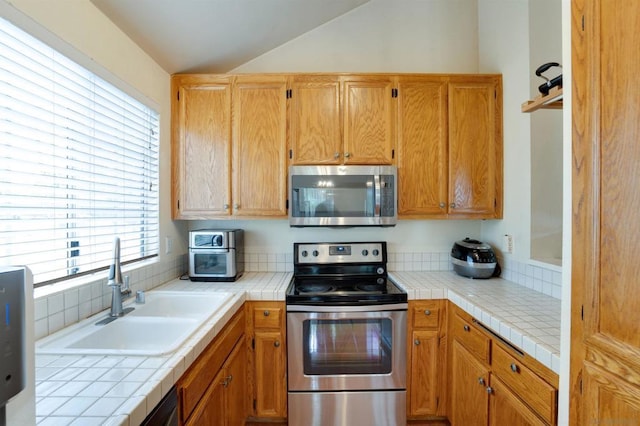 kitchen with appliances with stainless steel finishes, vaulted ceiling, tile counters, and sink