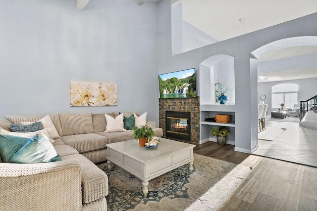 living room featuring a tile fireplace, built in shelves, dark hardwood / wood-style floors, and high vaulted ceiling