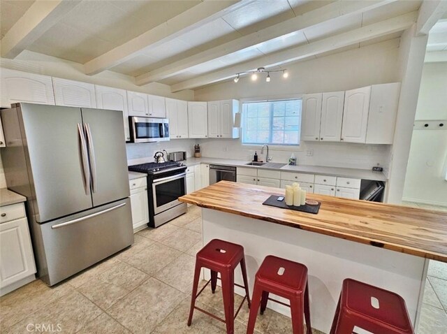 kitchen featuring white cabinets, a kitchen bar, wooden counters, and stainless steel appliances