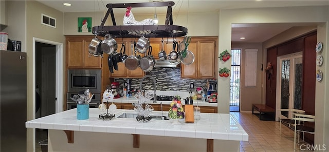 kitchen featuring tile counters, hanging light fixtures, backsplash, appliances with stainless steel finishes, and light tile patterned floors