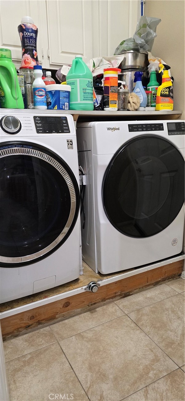 laundry area featuring independent washer and dryer, light tile patterned floors, and cabinets