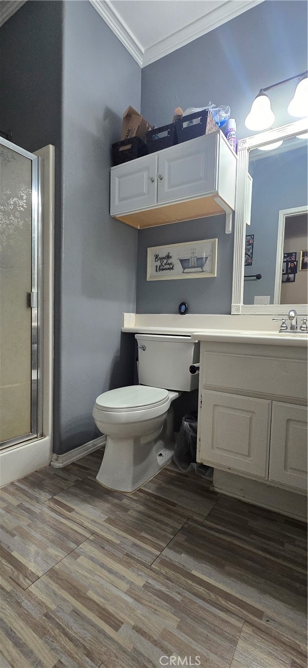 bathroom with hardwood / wood-style flooring, a shower with shower door, ornamental molding, vanity, and toilet