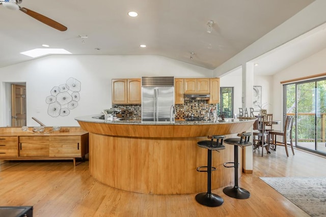 kitchen with lofted ceiling, light hardwood / wood-style flooring, backsplash, light brown cabinetry, and built in fridge