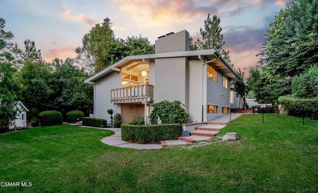 back house at dusk featuring a balcony and a lawn